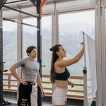 A gym coach instructs on whiteboard beside fitness equipment with mountain view.